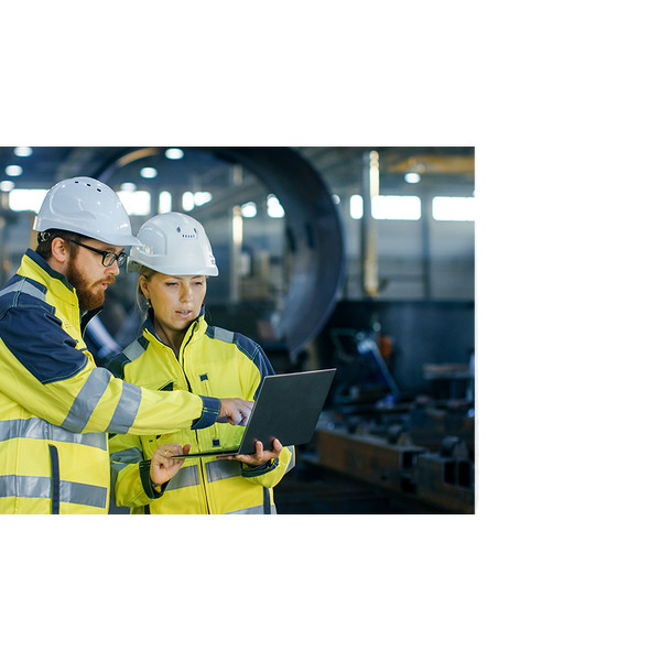 Zwei Industriearbeiter in Schutzausrüstung und Schutzhelmen diskutieren Daten auf einem Laptop in einer Fabrikumgebung.